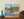 Painting of a landscape with trees and water on a wooden surface.