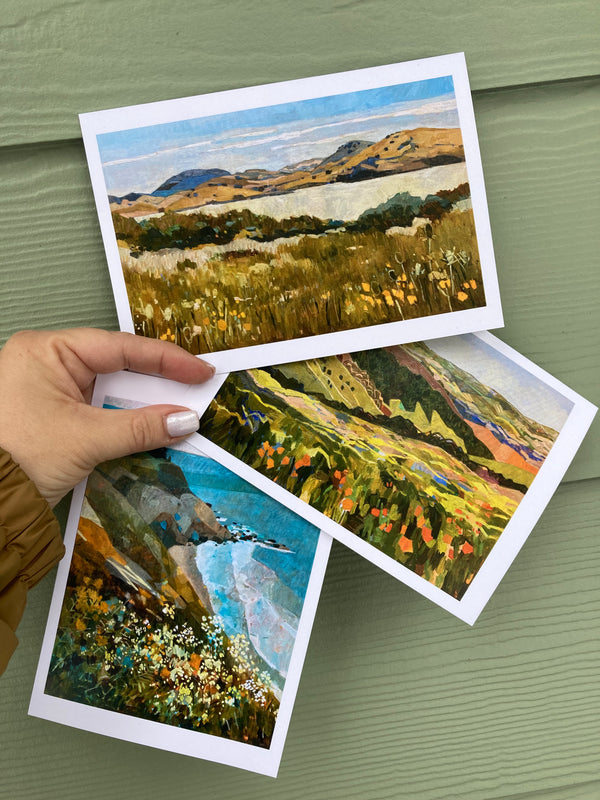 Hand holding three landscape postcards on a green surface