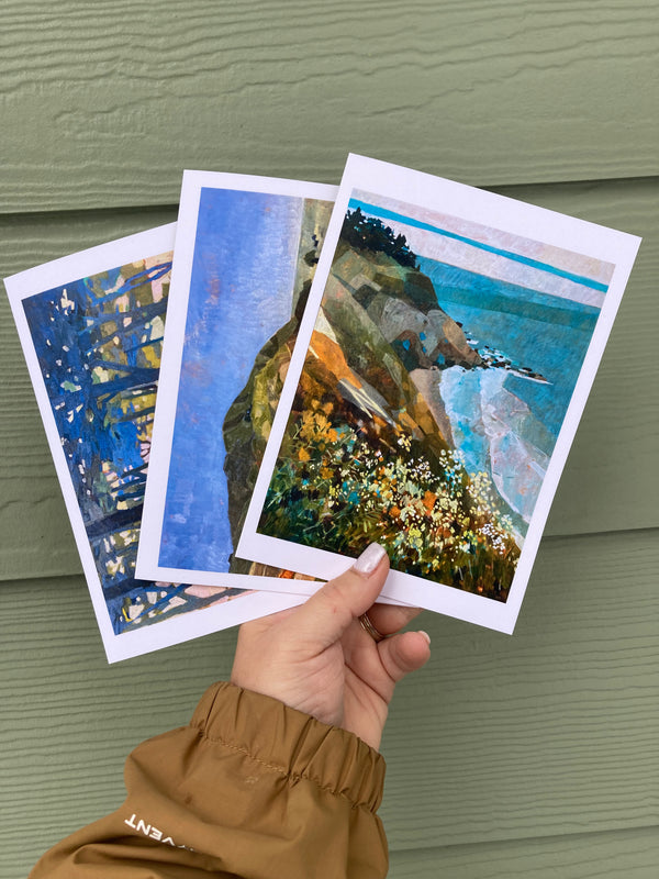Three artistic prints held by a person against a green wall.