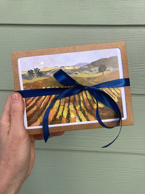 Hand holding a landscape painting wrapped with a blue ribbon against a green wooden background