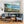 Living room with a large painting of a coastal scene above a blue sofa.