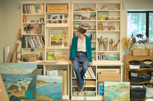 Woman standing in a room with bookshelves, artwork, and a printer.