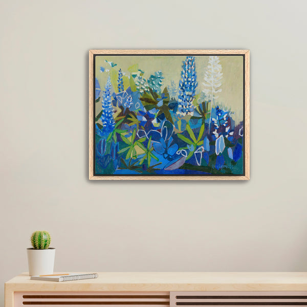 Framed floral painting on a wall with a cactus on a table below.