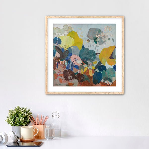 Framed abstract artwork on a white wall with a desk and decor items below.