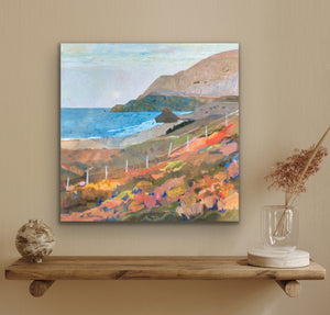 Painting of a coastal landscape on a wall above a wooden shelf with decorative items.