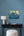 Decorative setup with a painting on a blue wall, black desk, white lamp, and white ottoman.