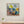 Framed abstract painting on a wall with a small potted plant below.