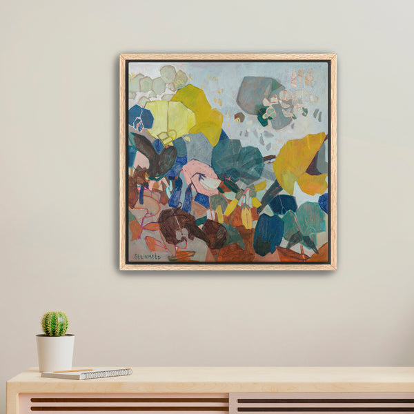 Framed abstract painting on a wall with a small potted plant below.